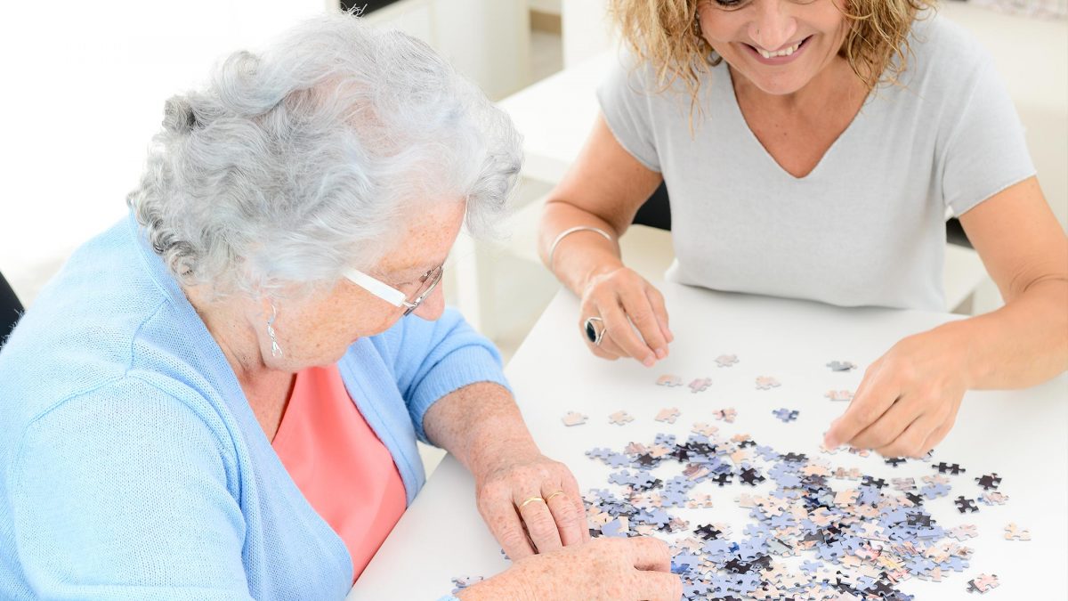 Seniorin/Rentnerin mit Hygge Betreuungskraft in Leipziger Wohnung spielen ein Puzzle zum Gedächtnistraining