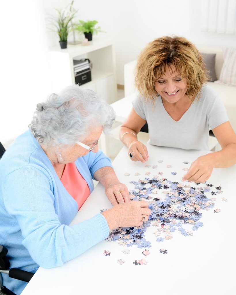 Betreuungskraft von Hygge Betreuung spielt mit einer Seniorin ein Puzzle, um die Gedächtnisleistung im Alter zu fördern, ihr Gesellschaft zu leisten und miteinander Zeit zu verbringen