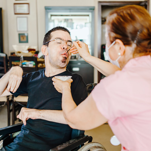 Betreuungskraft hilft Menschen mit Behinderung als Familien-Alltagshilfe im Rollstuhl beim Essen / Hygge Betreuung