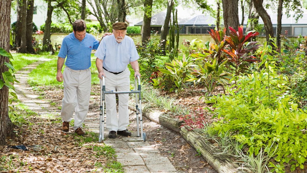Hygge Betreuungskraft unterstützt Senior beim Laufen, welcher am Rolllator geht.