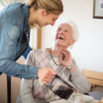 Hygge Betreuung - Tagespflege - junge Frau schenkt Seniorin einen Kaffee ein, beide lächeln.